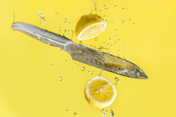 fresh organic lemon cut with a knife in water drops isolated over bright yellow background, healthy...