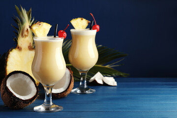 Tasty Pina Colada cocktails and ingredients on blue wooden table, space for text - obrazy, fototapety, plakaty