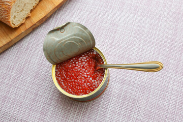 Caviar is in a jar. Close-up of red caviar and a spoon. In the background there is bread. - 477912867