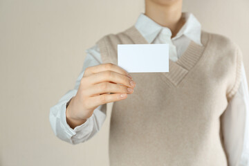 Woman holding white business card on beige background, closeup