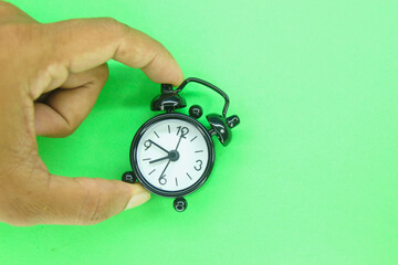 a finger holding a black alarm clock with a green background