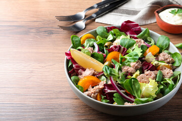 Bowl of delicious salad with canned tuna and vegetables on wooden table, space for text