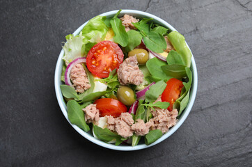 Bowl of delicious salad with canned tuna and vegetables on black table, top view
