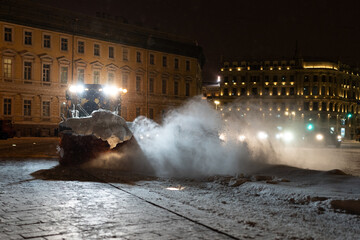 Tractor with rotary sweeper clearing city street at night after heavy snowfall. Clearing city by...