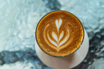 cup of hot latte art coffee on glass table in morning sun light, relax time