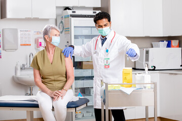 Obraz premium A Young Indian Male Medical Doctor Disposes of Syringe Needle Safely in Sharps Collector after a Covid-19 Vaccine Injection Wearing Gloves, Mask and Generic ID Badge in Hospital or Health Clinic. 