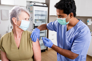 A Young Indian Male Medical Nurse Administering a Covid-19 Vaccine with a Syringe Needle to an...