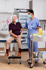 A Young Indian Male Medical Nurse Consults with an Elderly Senior Male Patient about Covid-19...