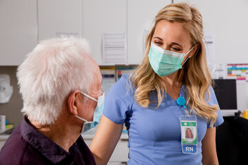 A Young White Female Medical Nurse Consults with an Elderly Senior Male Patient about Covid-19...
