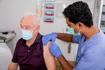 A Young Indian Male Medical Nurse Administering a Covid-19 Vaccine with a Syringe Needle to an...