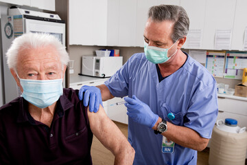 A White Male Medical Nurse Administering a Covid-19 Vaccine with a Syringe Needle to an Elderly...