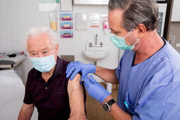 A White Male Medical Nurse Administering a Covid-19 Vaccine with a Syringe Needle to an Elderly...