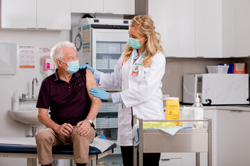 A Young White Female Medical Doctor Administering a Covid-19 Vaccine with a Syringe Needle to an...