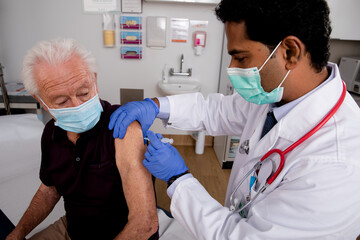 A Young Indian Male Medical Doctor Administering a Covid-19 Vaccine with a Syringe Needle to an...