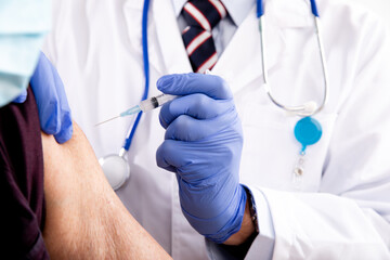 Covid-19 Vaccine Injection Close Up by a Male Doctor with Gloves using a Syringe Needle with Elderly Senior Male Patient wearing Masks and Generic ID Badge in Hospital or Health Clinic. 