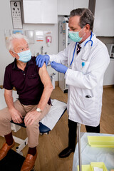 A White Male Medical Doctor Administering a Covid-19 Vaccine Injection with a Syringe Needle to an...