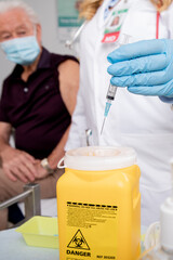 Safe Disposal of Syringe Needle in Sharps Collector after Administering a Covid-19 Vaccine. Close Up of Female Doctor Wearing Generic ID Badge, Lab Coat, Gloves and Mask in Hospital or Health Clinic. 