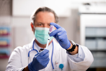 A White Male Medical Doctor Extracting a Covid-19 Vaccine with a Syringe Needle Wearing Generic ID...