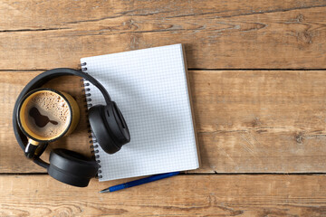 Blank notebook with coffee cup, pen and headphones on wooden table. Writing notes, planning concept