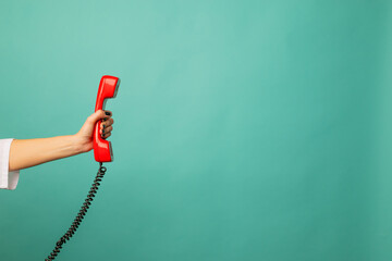Closeup view of woman holding red corded telephone handset on blue background, space for text. Hotline concept - obrazy, fototapety, plakaty
