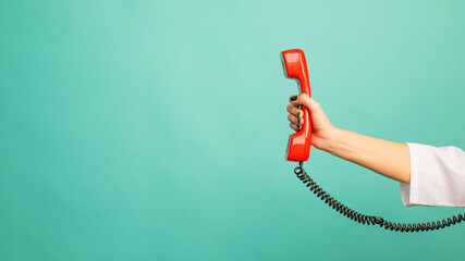 Closeup view of woman holding red corded telephone handset on blue background, space for text....