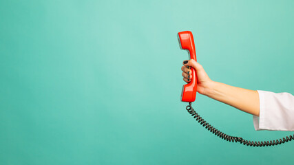 Closeup view of woman holding red corded telephone handset on blue background, space for text. Hotline concept
