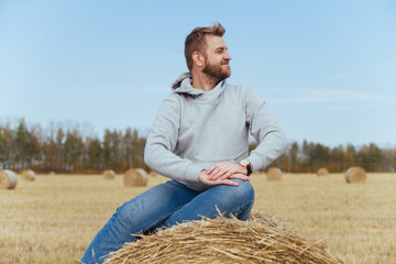 Naklejka na ściany i meble Happy man with a beard in a hoodie sits on a haystack