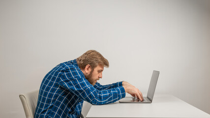 Beard emotional man in slouching position sitting in office room, working with laptop