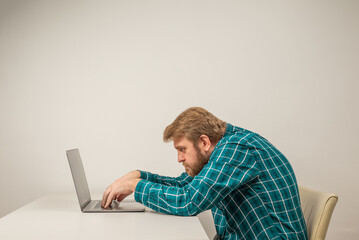 Beard emotional man in slouching position sitting in office room, working with laptop
