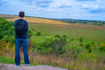 Back of a man tourist with a backpack on the background of a beautiful field and hills