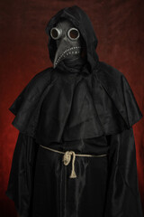 Dark black figure of a man in a mask of plague doctor stands on red background