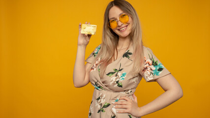 Portrait of a lovely young woman showing credit card isolated over yellow background