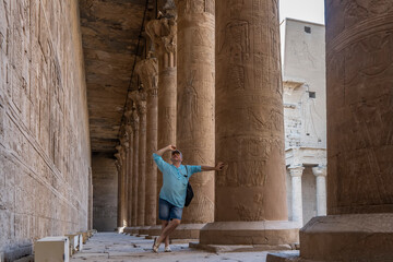 A man stands in the ancient Egyptian temple of Horus.  He leans on a column with his hand, looks...