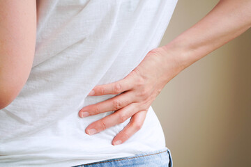 woman in white t-shirt touch her waist and hold lower back which suffering from back pain or back ache