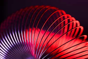 Closeup of coiled metal spring with sufficiently high strength and elastic properties in neon light over dark background. Macro photo, selective focus. - obrazy, fototapety, plakaty