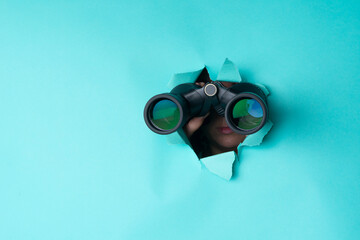 Female hand holds black binoculars on a blue background. Journey, find and search concept. Banner.