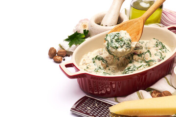 Delicious meatballs with spinach in a creamy sauce in baking dish on white background