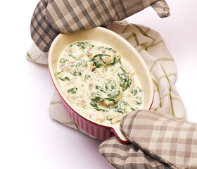 Delicious meatballs with spinach in a creamy sauce in baking dish on white background