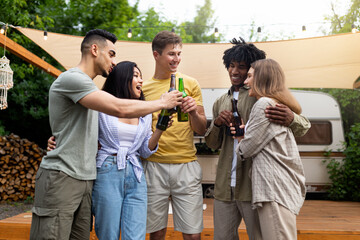 Group of young multiracial people drinking beer on camping trip, toasting with alcohol bottles, joking and laughing
