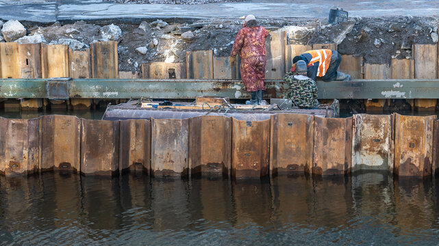 three men from the raft perform restoration work on the river bank. the technology of repairing the river embankment in the city. a place to print the text. background picture.