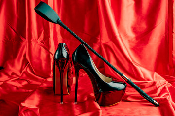 Adult sex games. BDSM items. Patent Fetish Extreme High Heel Stiletto Heels and whip on a red satin...