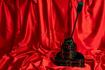 Adult sex games. BDSM items. Leather straps handcuffs, belt and whip on a red satin sheet.
