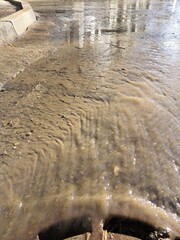 the pattern of water in the form of a stream flowing down dirty asphalt in spring as a result of snowmelt