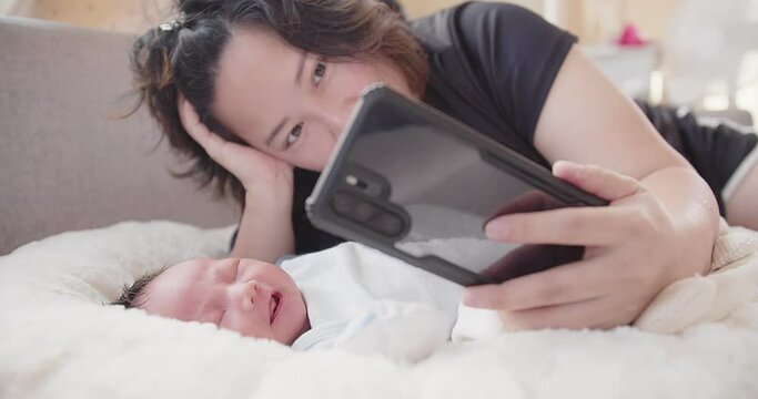 happiness young Asian mother and pretty newborn baby infant girl video call to father or relatives in a bed at home, family, children, parenthood, childhood,  technology, motherhood, love, connection