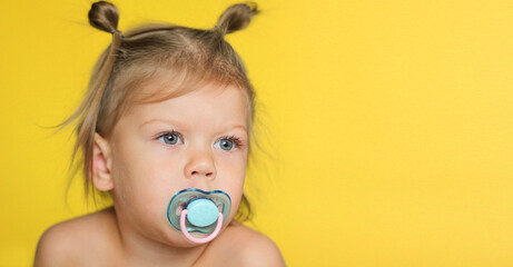 Portrait of cute caucasian child kid little girl of 2 years with pacifier in mouth on yellow...