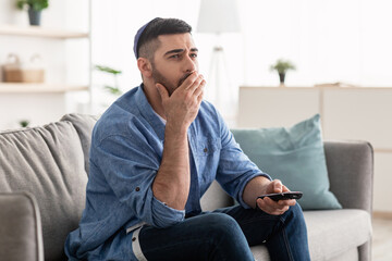 Bored jewishman watching television sitting on couch