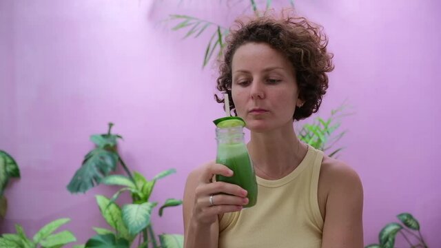 Curly lady drinking green refreshing vitamin detox smoothie shake for wellness lifestyle, health and weight loss