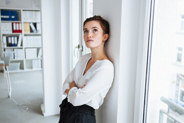 Serious young businesswoman standing deep in thought