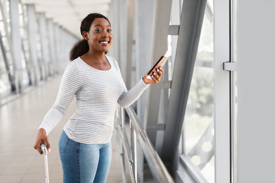 Happy excited black woman traveling, looking out window in airport