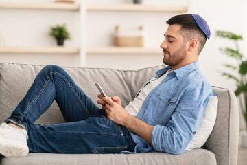 Profile of jew man using mobile phone sitting on couch